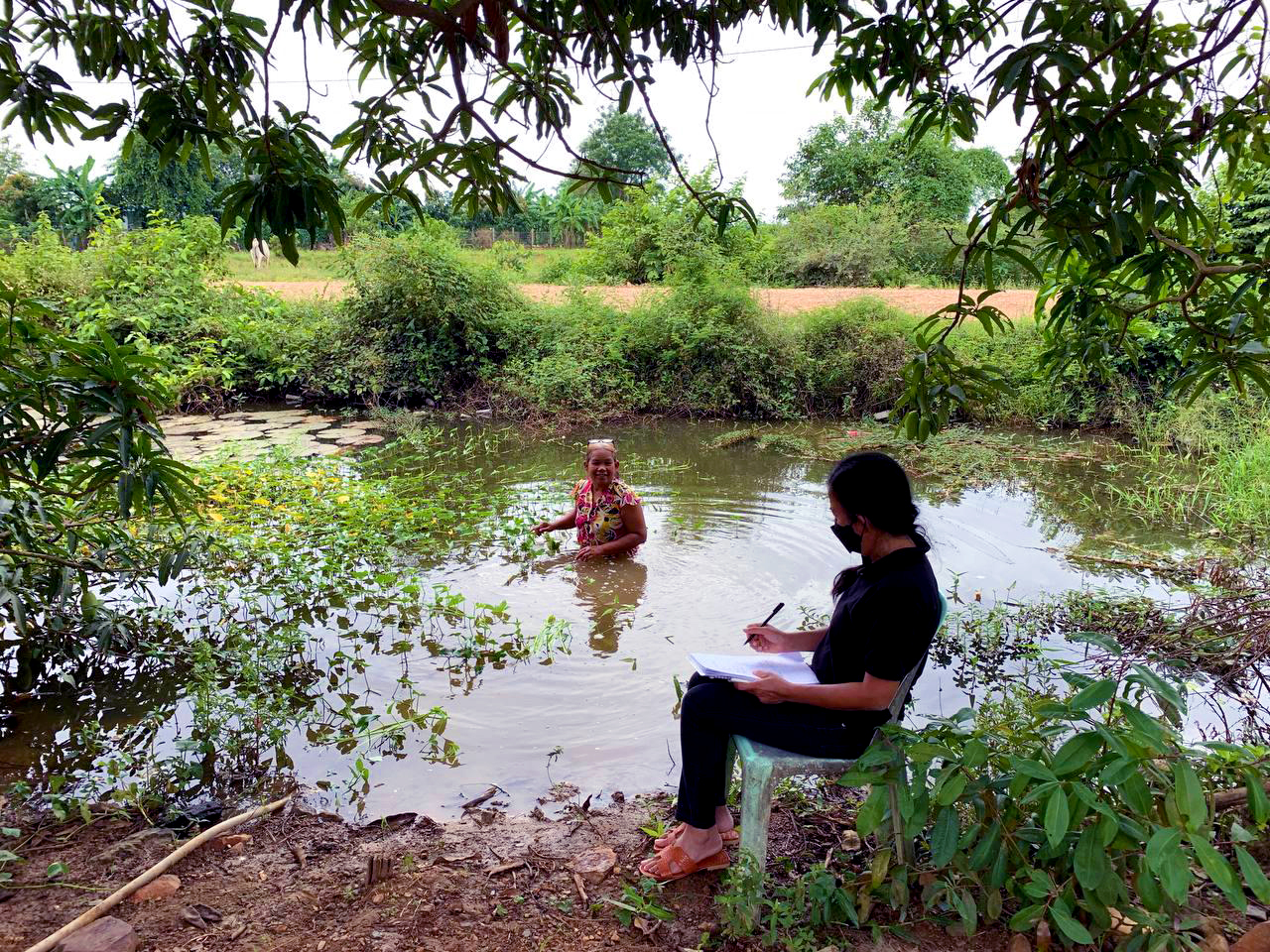 a person in waist-deep water in jungle with another person looking on, courtesy
