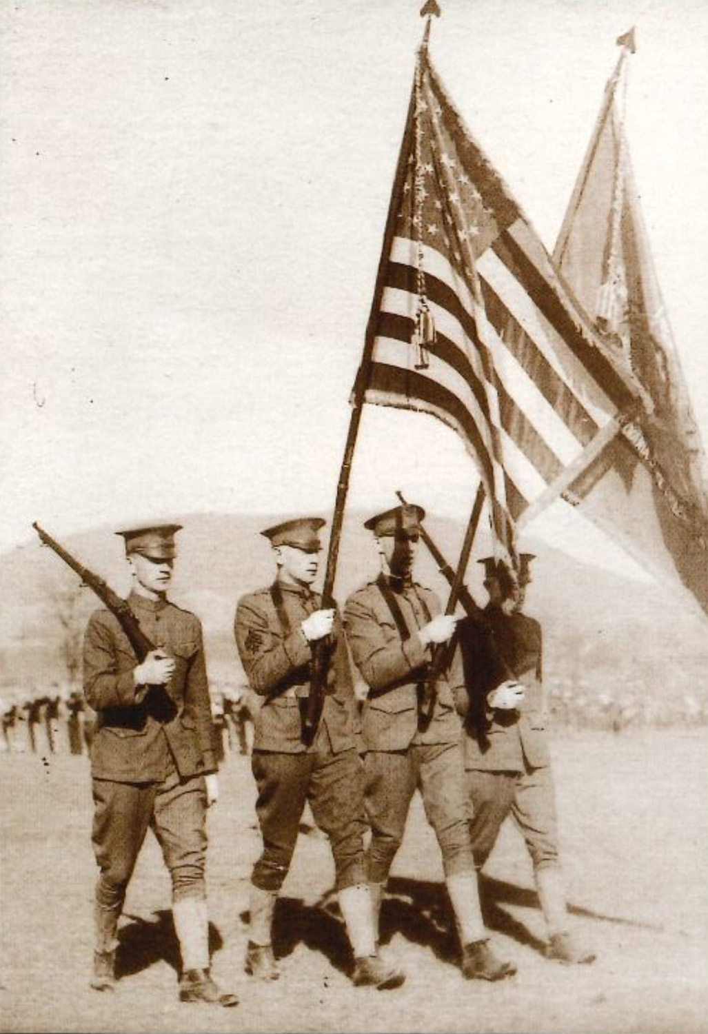 sepia photo of men in uniform marching with flag by Penn State Archives