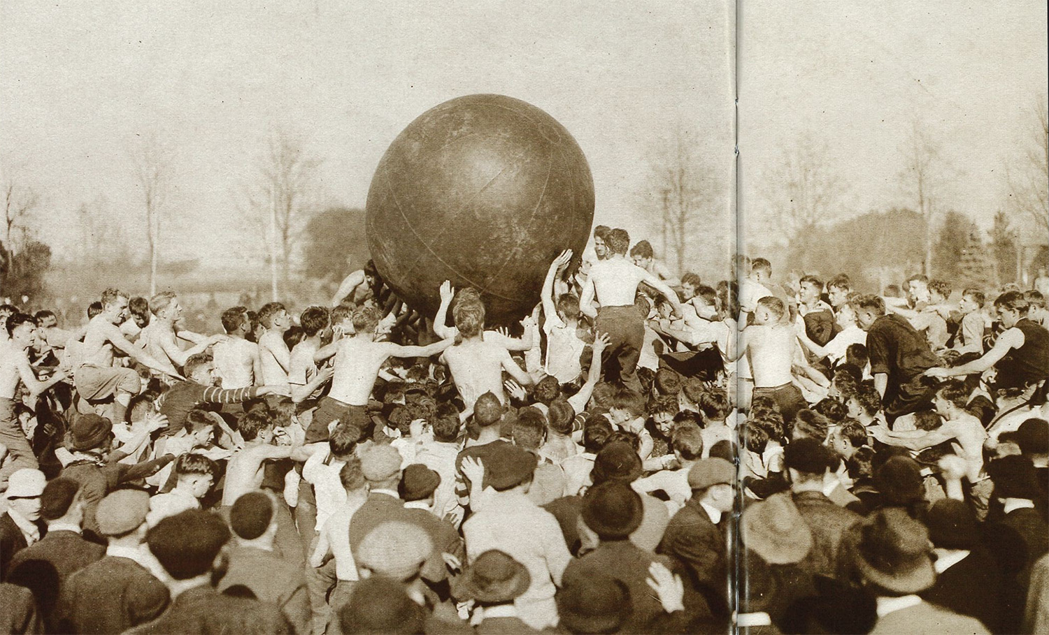 sepia photo of young men pushing a giant leather inflatable ball by Penn State Archives