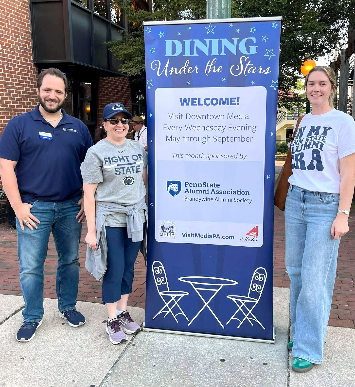 alums standing beside Dining Under the Stars signage, courtesy