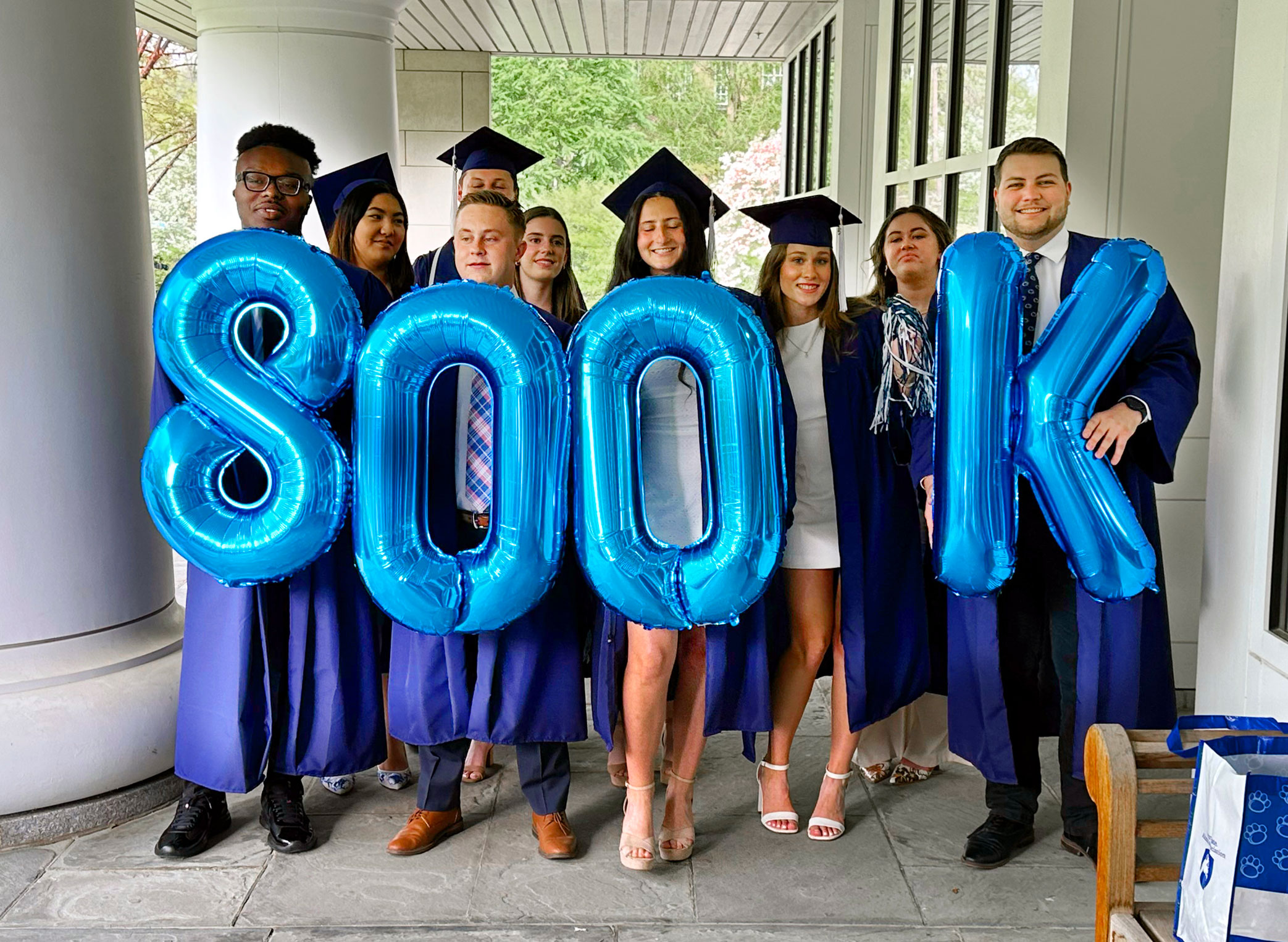 photo of students in caps and gowns holding up blue balloons that spell out 800K, by Ryan Jones '95 Com