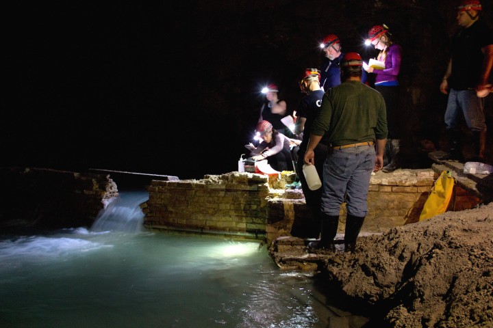 group of scientists wearing head lamps and taking notes beside flowing water in a cave, photo by Zena Cardman