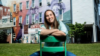 Pamela Snyder Esters sitting on green chair in front of a building with a colorful mural, by Cardoni