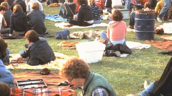 photo of students sitting on blankets on the HUB lawn playing backgammon and listening to music with stage in the background photo by Patrick Mansell