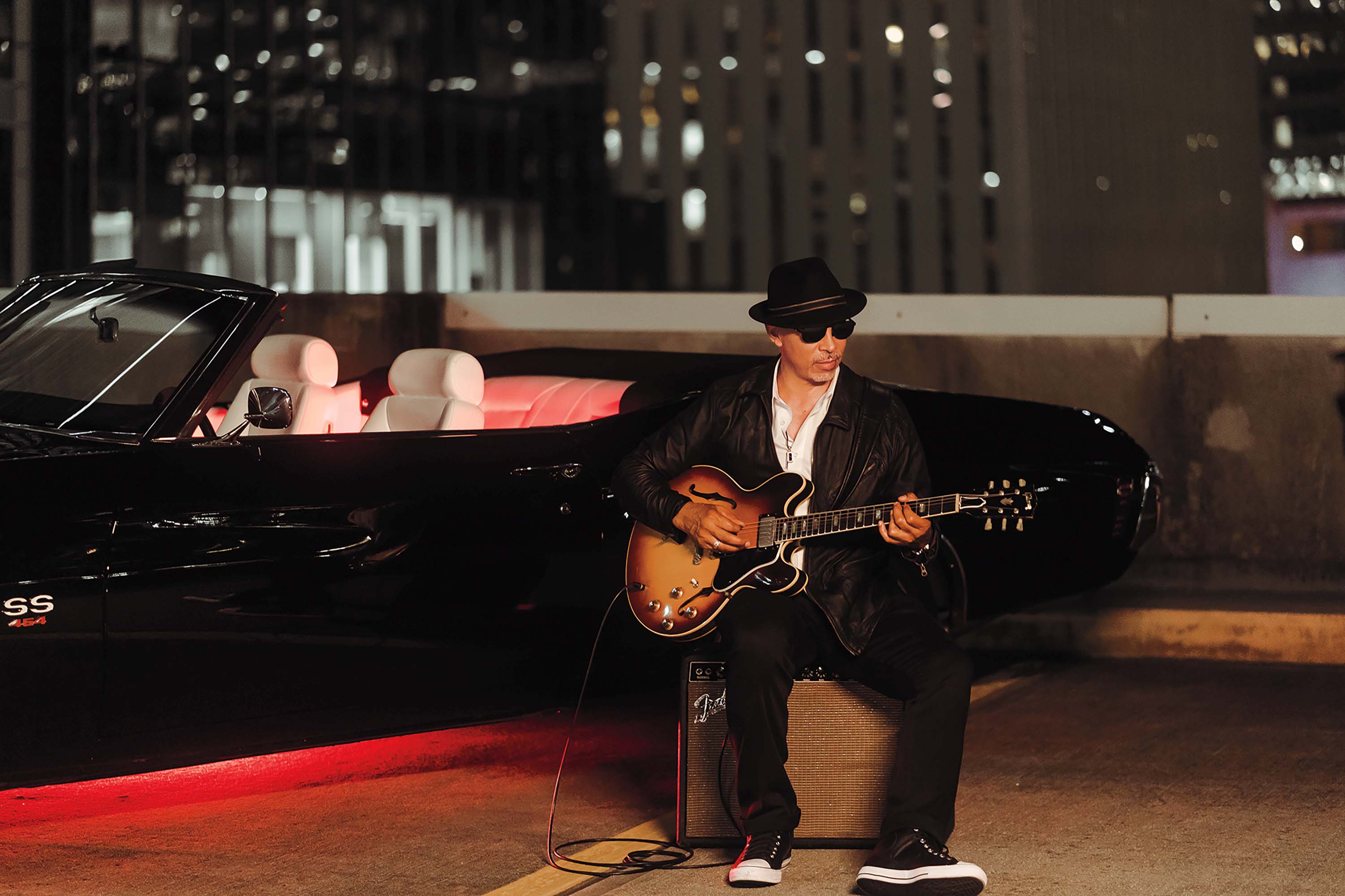Gene Woods playing guitar in front of sportscar