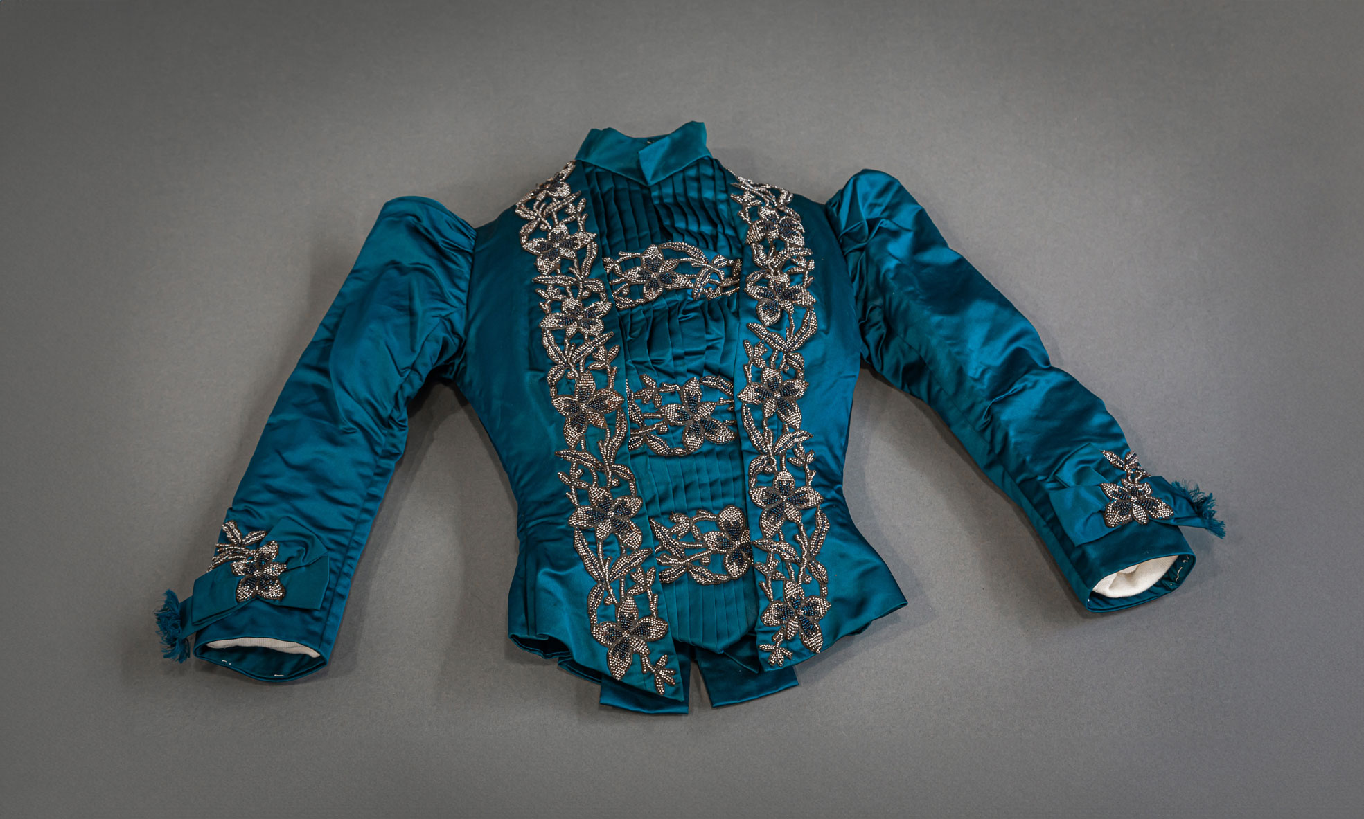 photo of a peacock blue silk-satin dinner jacket with intricate beadwork and a banded collar with pleating on the bust, garment from the Penn State Fashion Archive photographed by Nick Sloff '92 A&A