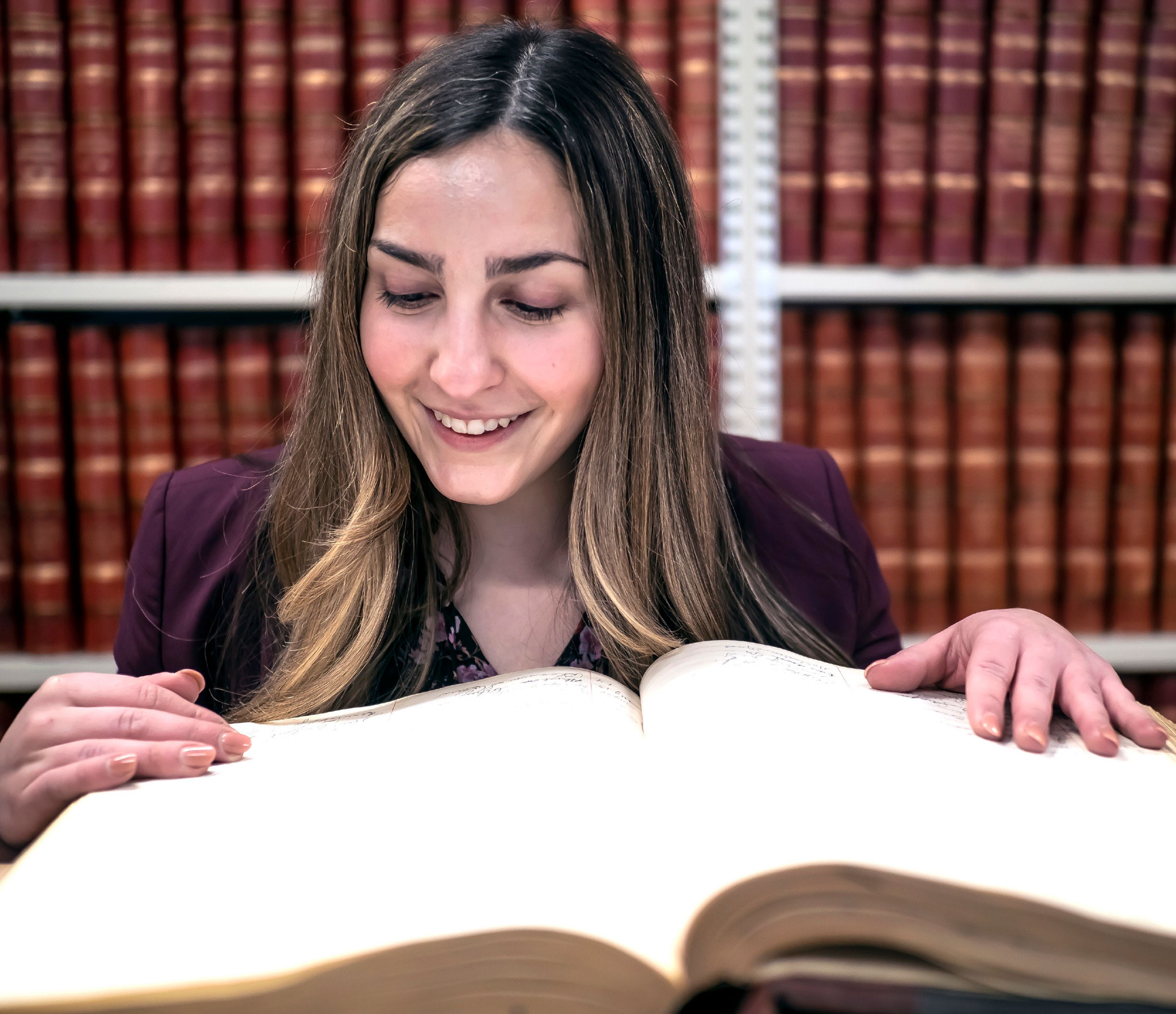photo of Miller looking at a thick book in front of bookshelves, courtesy