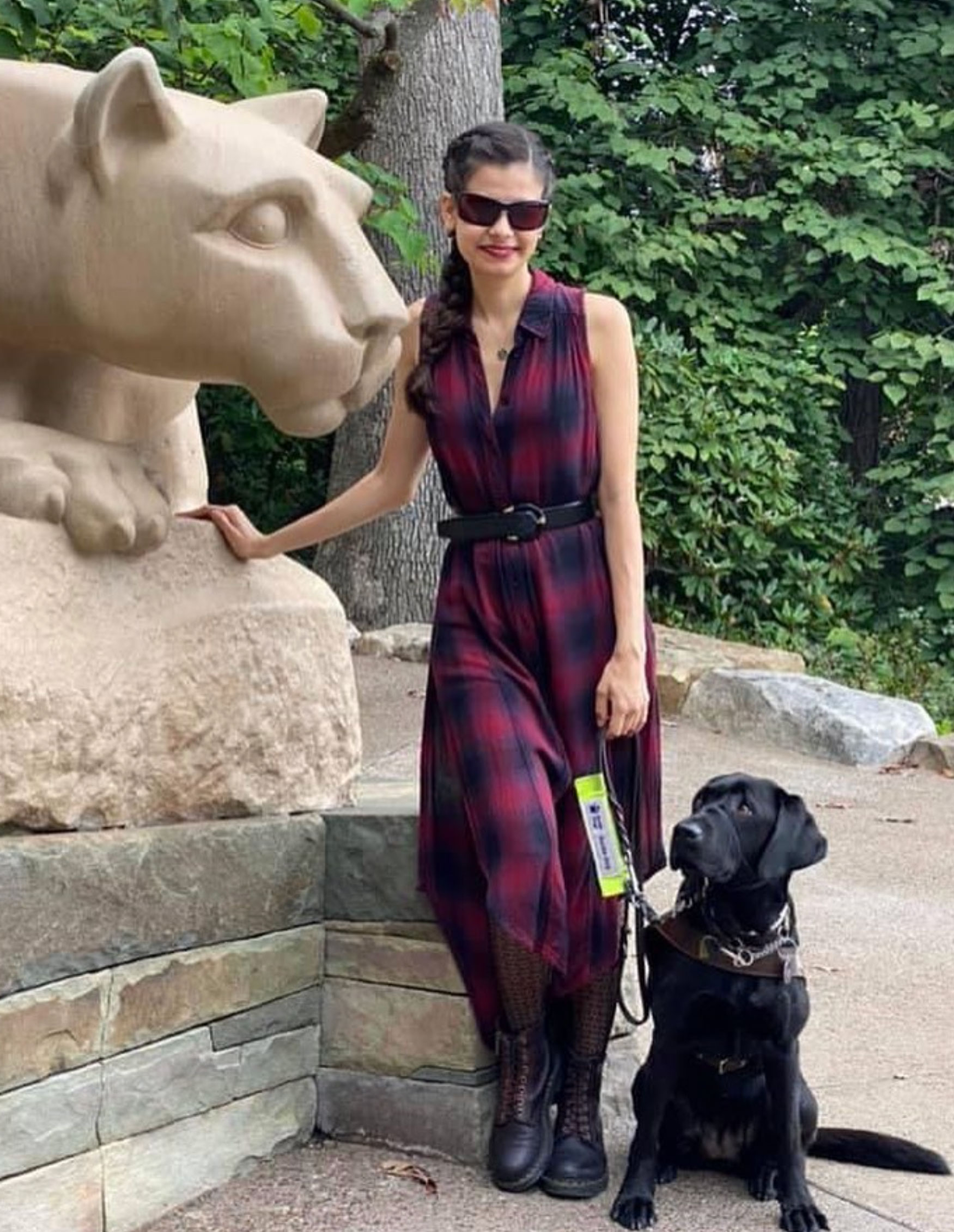 Loberti in a red and blue plaid dress standing beside the Nittany Lion statue with her black Labrador, Ingrid, photo courtesy