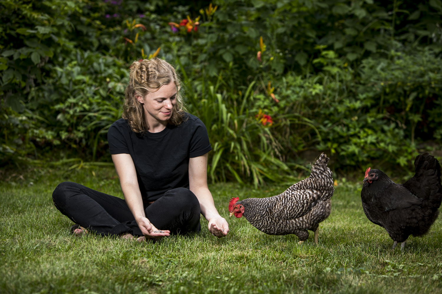 Cardman sitting in the grass with several of her chickens, photo by Steve Boyle