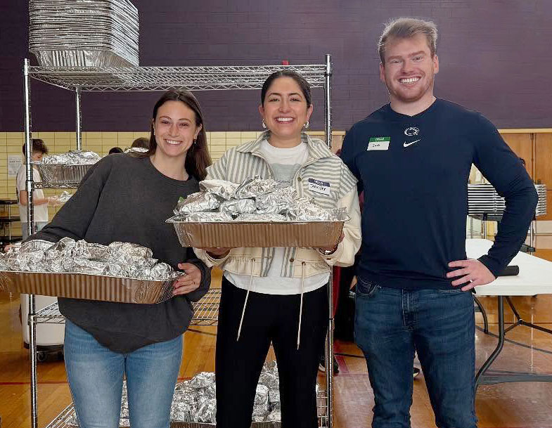 three alums from the Chicago chapter in a kitchen holding trays of foil wrapped sandwiches, courtesy