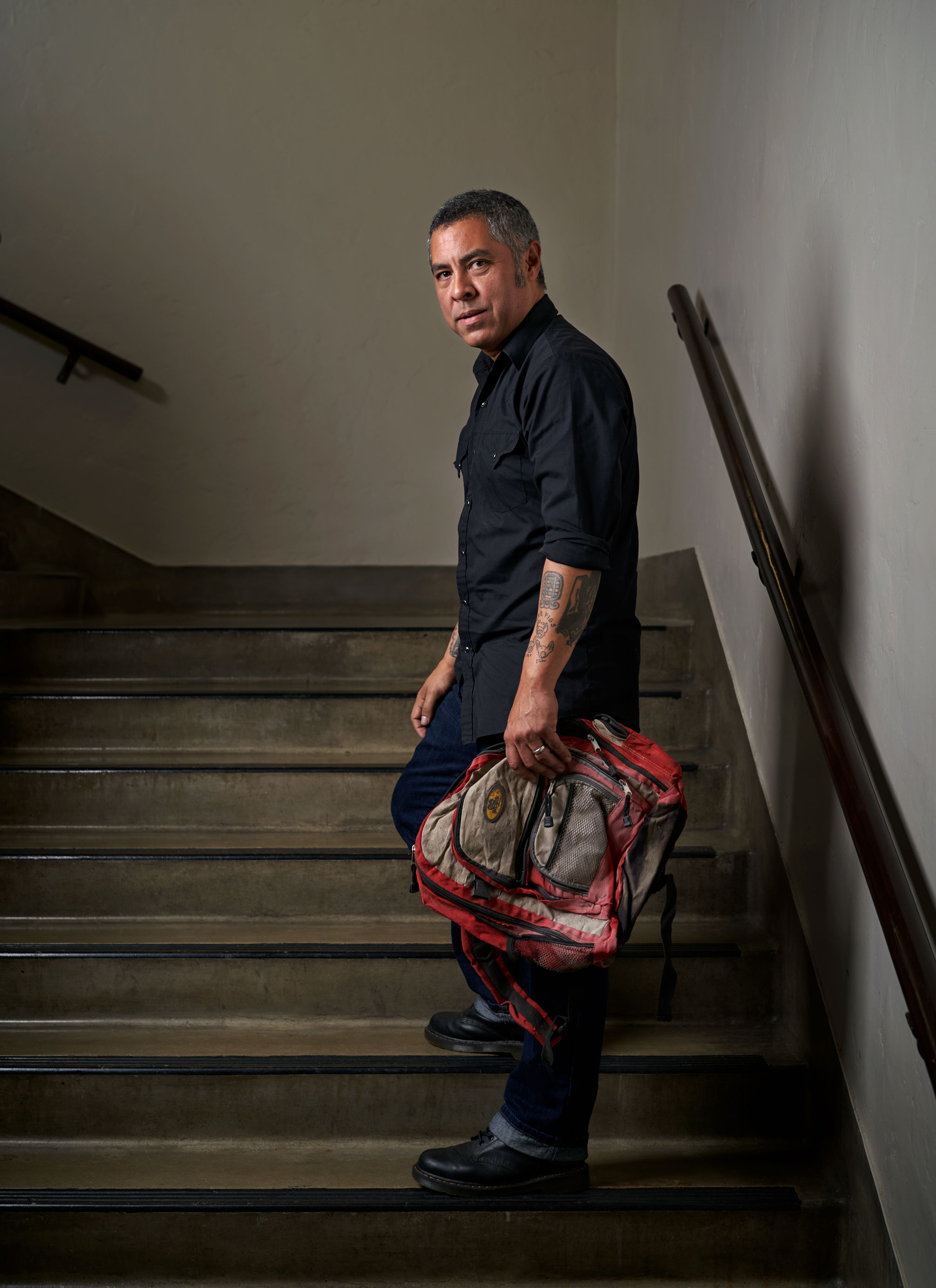 De Leon holding a backpack standing on steps, photo by Gregg Segal