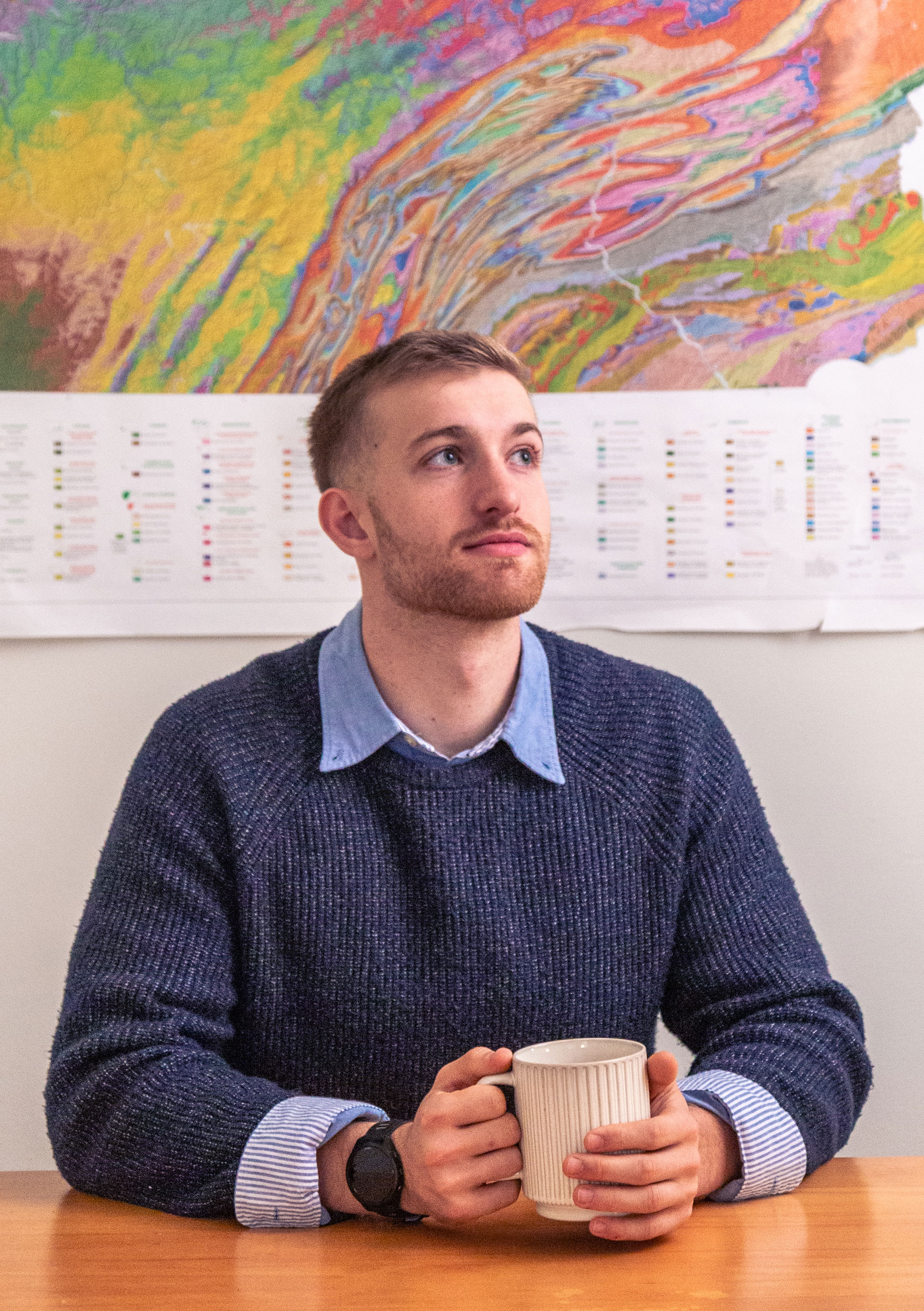 Hollingham seated at a table with a coffee mug before a vibrantly colored map of Pennsylvania, photo by Nick Sloff '92 A&A