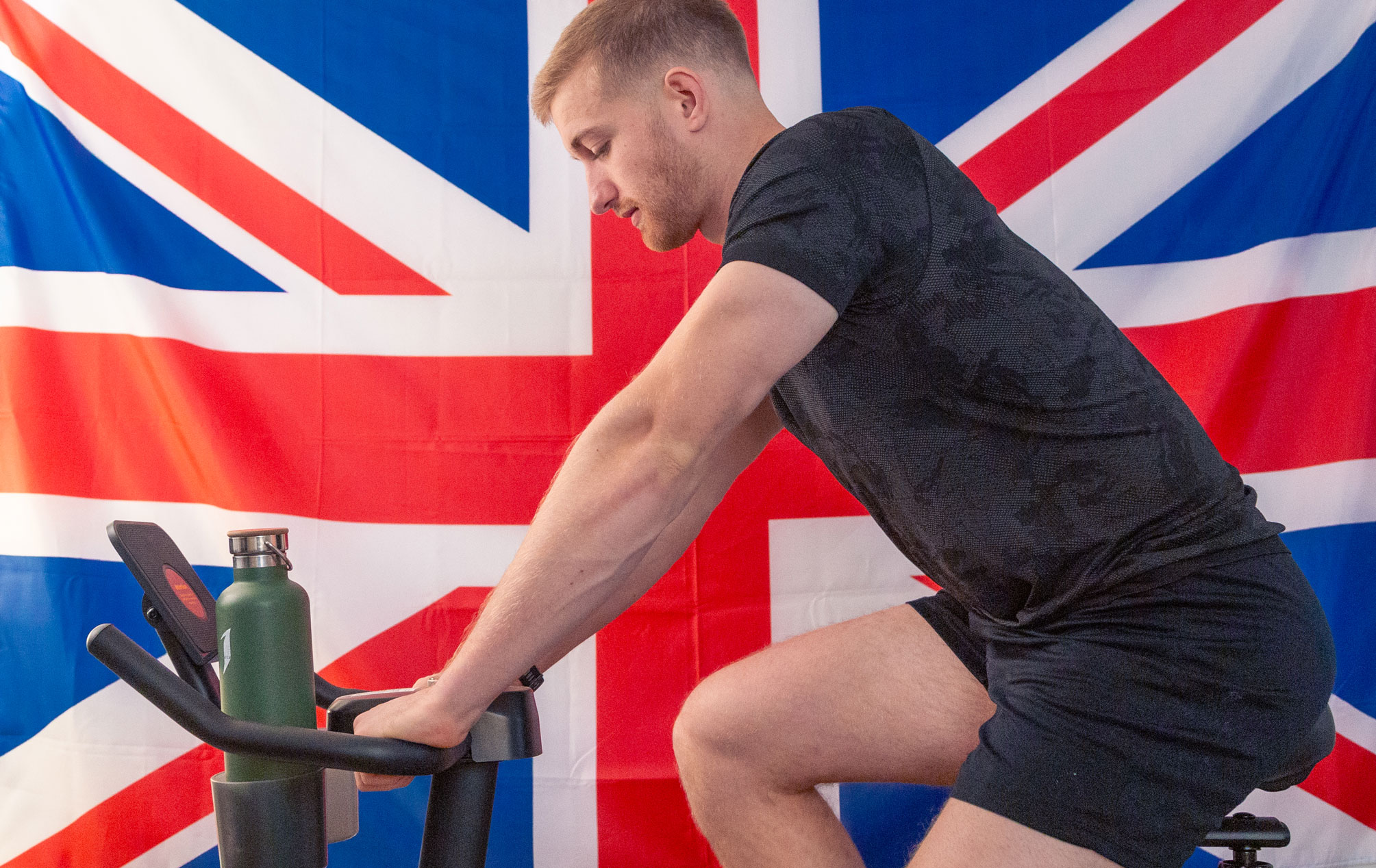 photo of Hollingham on a stationary bike in front of a UK flag by Nick Sloff '92 A&A