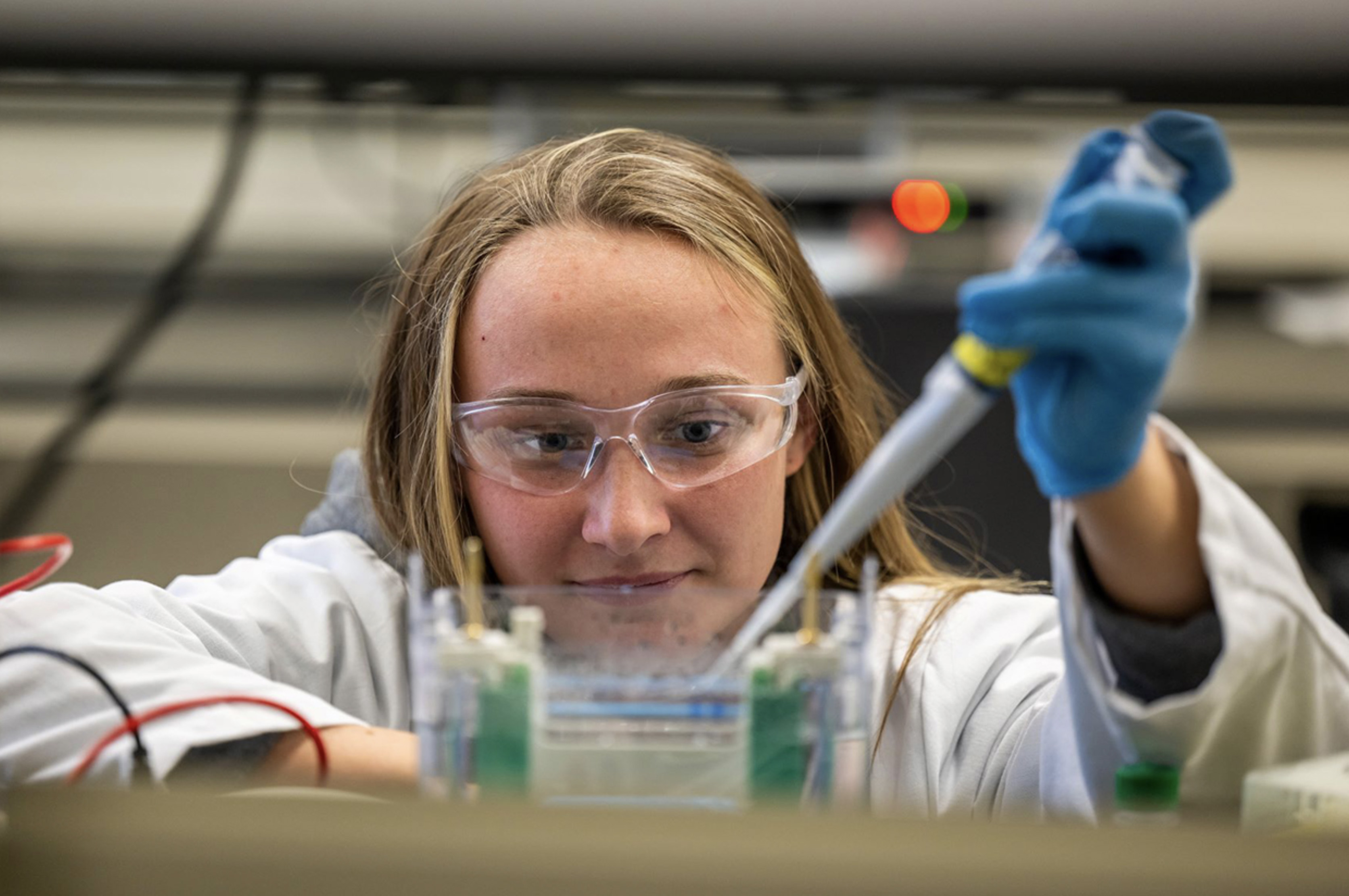 photo of a student in a science lab wearing safety glasses and lab coat while extracting liquid from a container by Penn State Behrend