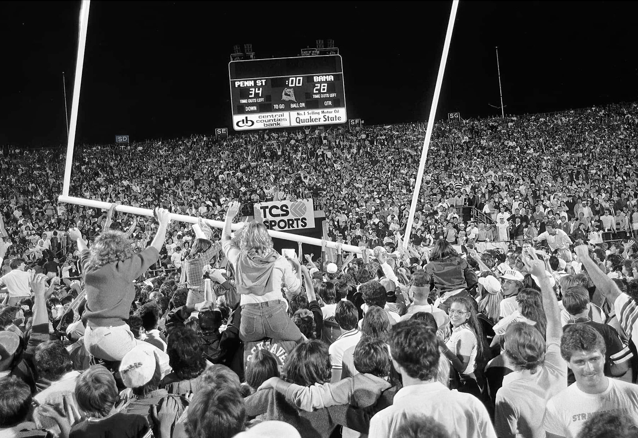 black and white photo of a huge group of fans at Beaver Stadium toppling the goal posts by Pat Little