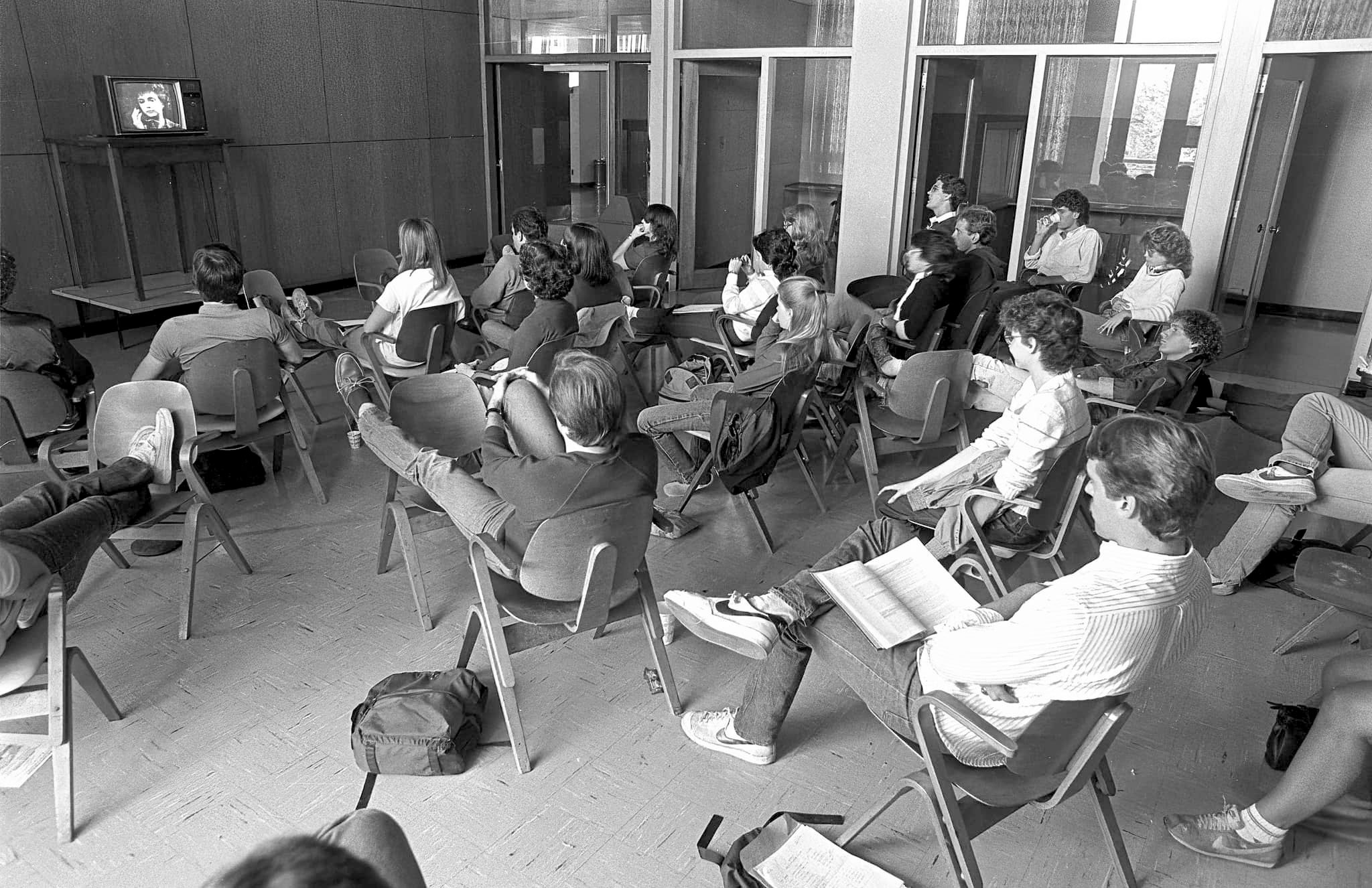 black and white photo of a group of students seated in desks all watching a small TV in the HUB by Pat Little