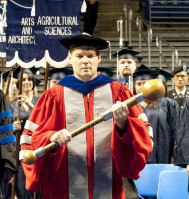 graduate holding the university mace during ceremony, photo by Patrick Mansell/Penn State