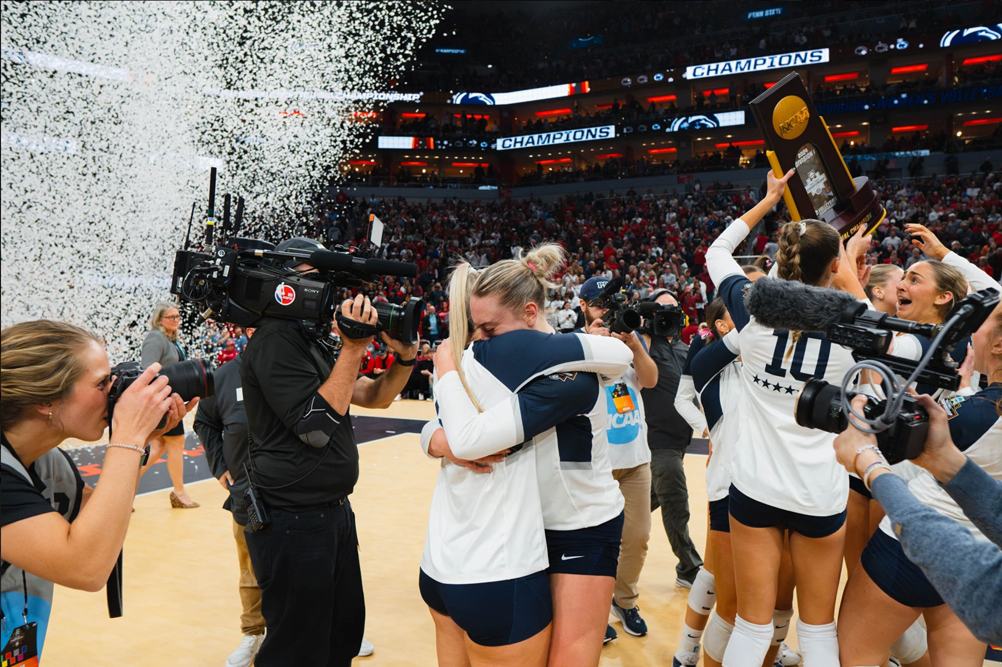 Nittany Lion women's volleyball players embrace after national title win as camera people film them and confetti rains down, photo by Penn State Athletics