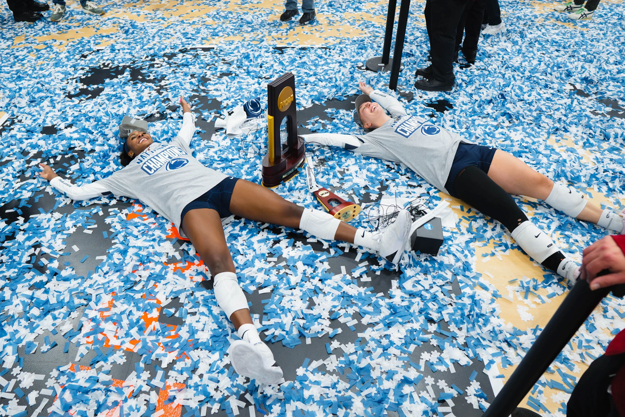 Nittany Lion women's volleyball players make confetti angels on the court with NCAA trophy, photo by Penn State Athletics