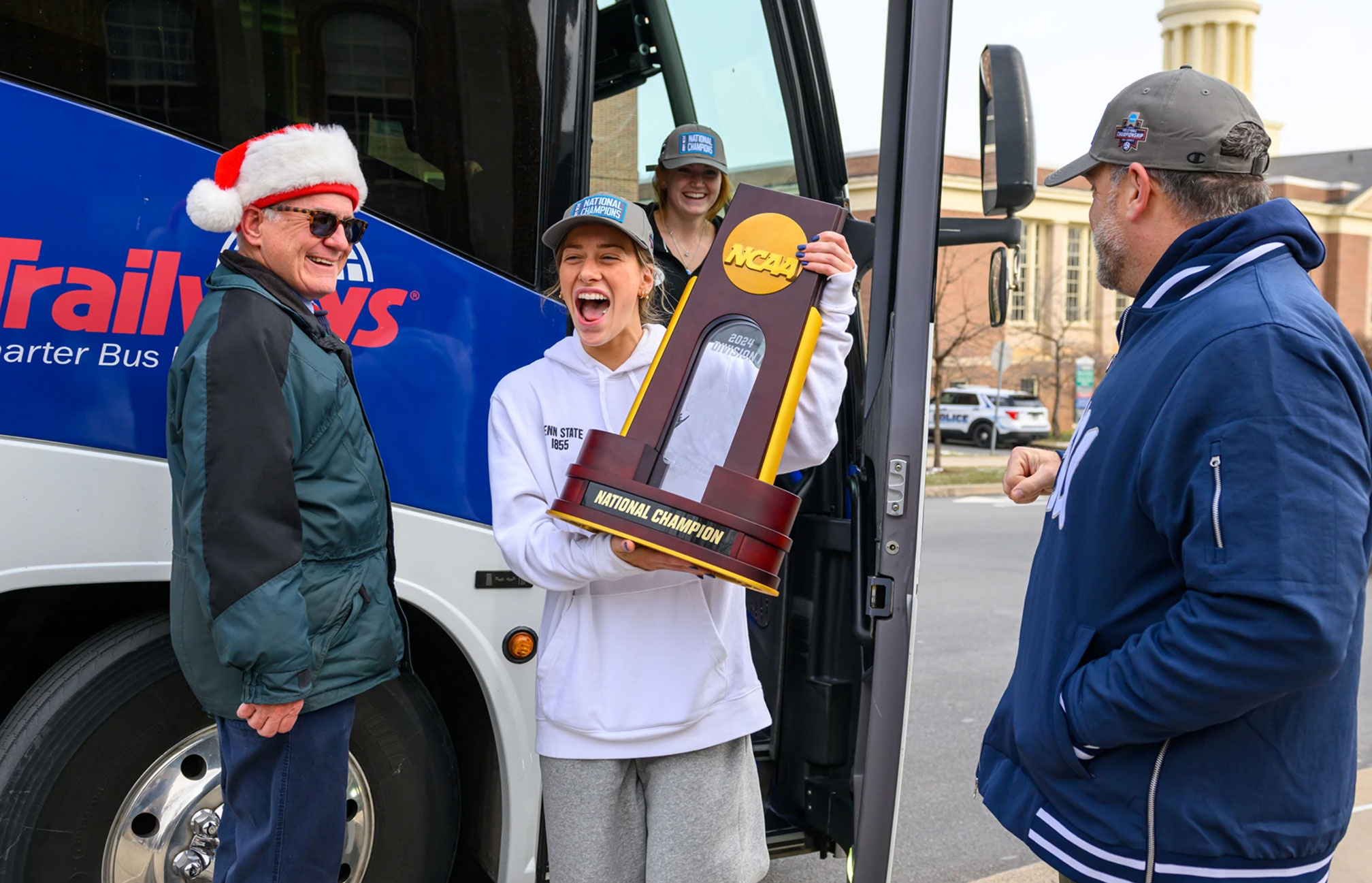 a Nittany Lion women's volleyball player holding up the NCAA trophy after exiting charter bus upon returning home, photo by Penn State Athletics