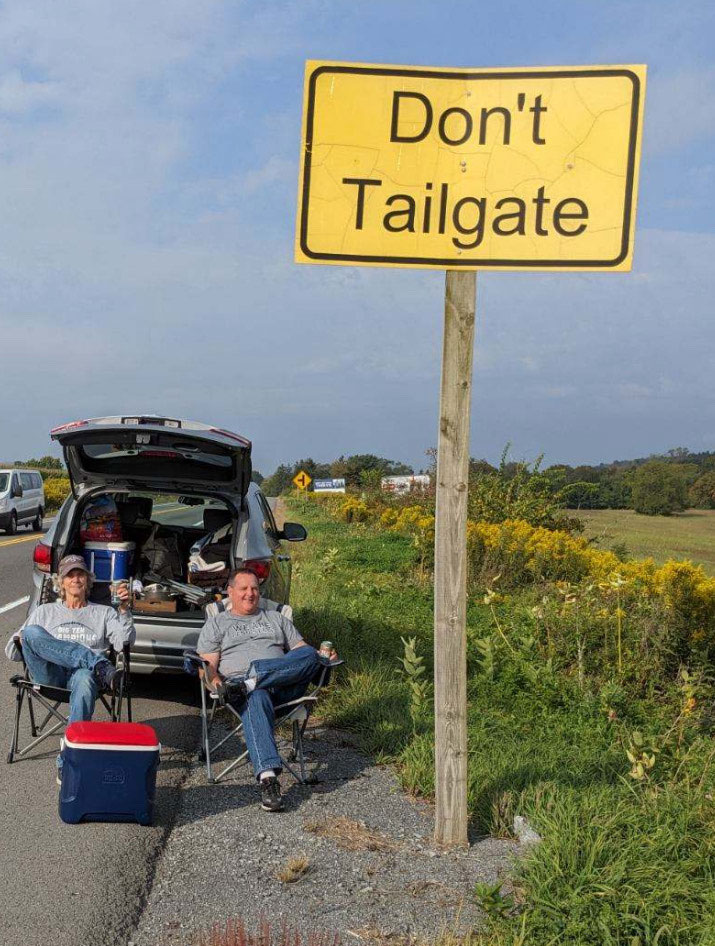 two people sitting in camping chairs tailgating on the side of the road, courtesy