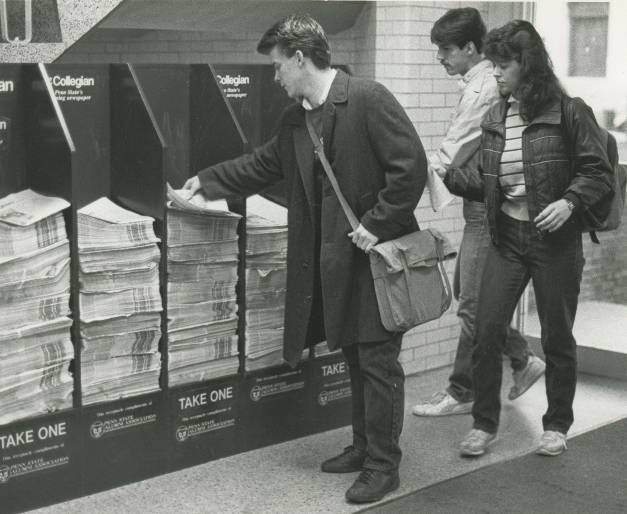 black and white photo of students picking up copies of the Collegian from newsstand, courtesy Collegian