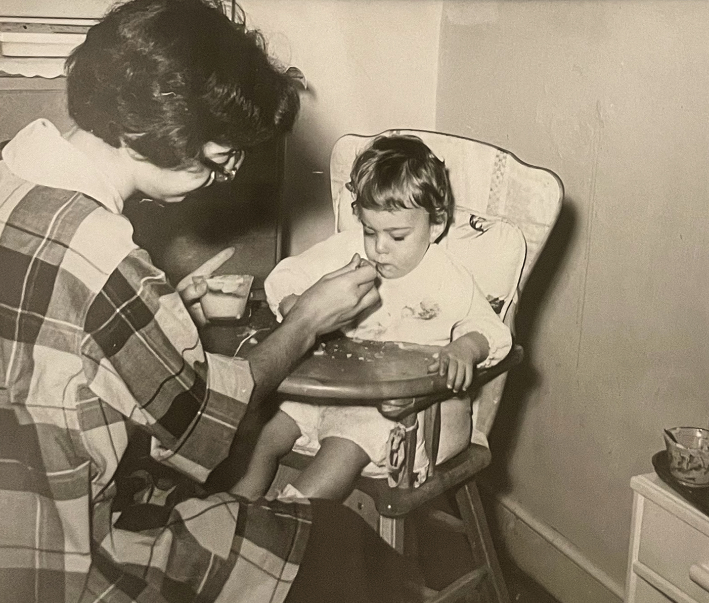 sepia photo of a baby in a wooden highchair being fed, courtesy Nancy Taylor