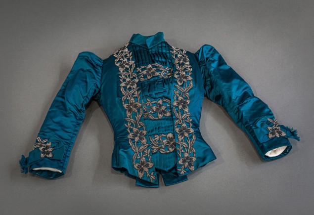 photo of a peacock blue silk-satin dinner jacket with intricate beadwork and a banded collar with pleating on the bust, garment from the Penn State Fashion Archive photographed by Nick Sloff '92 A&A