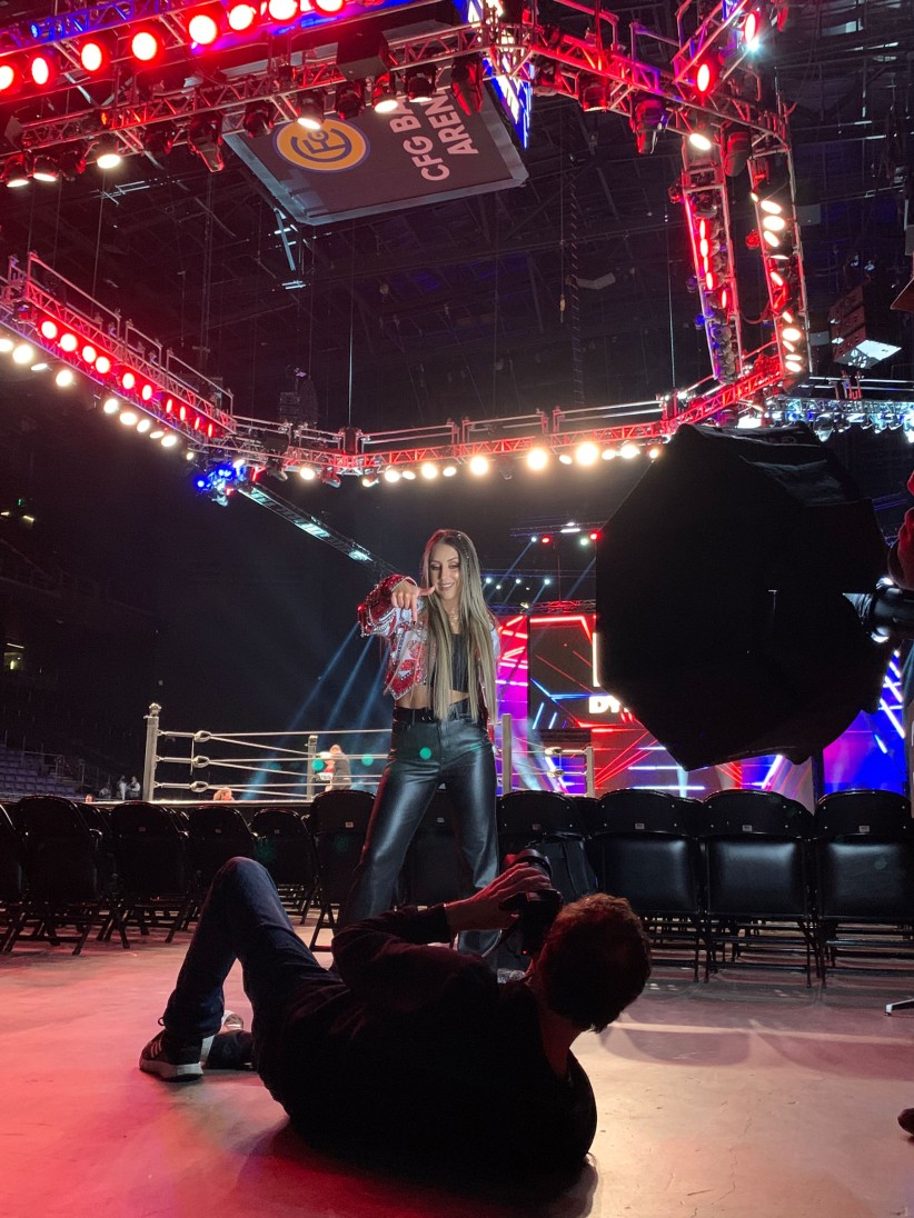 Britt Baker under arena lights with a photographer on the floor in front of her capturing a shot, by Ryan Jones '95 Com