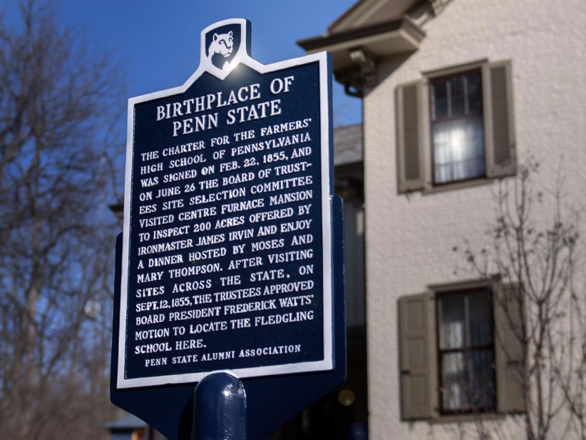 Penn State historical marker sign reading "Birthplace of Penn State" with building and blue sky in background, by Patrick Mansell
