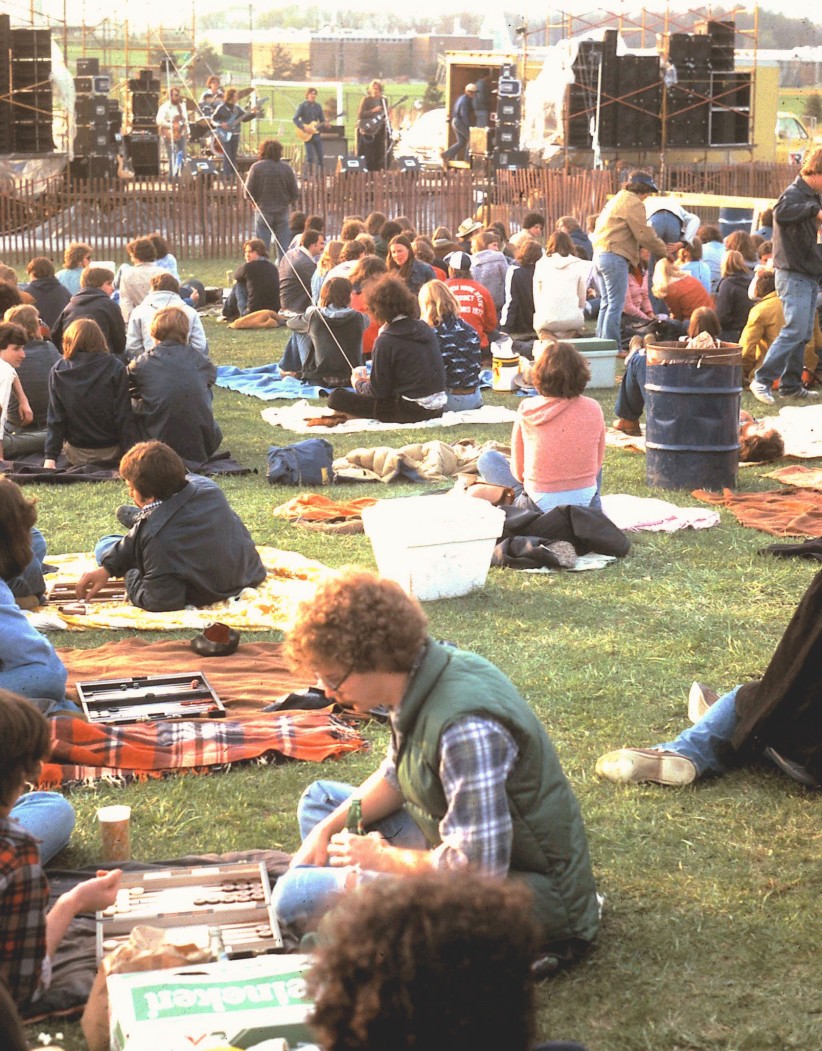 photo of students sitting on blankets on the HUB lawn playing backgammon and listening to music with stage in the background photo by Patrick Mansell