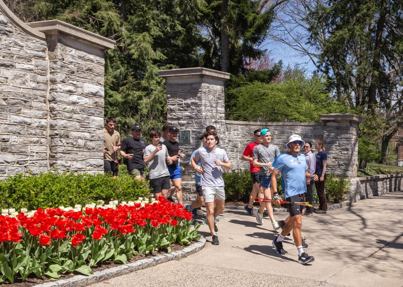 photo of Paul Johnson running through the gates below Old Main onto College Ave with other runners behind him by Nick Sloff '92 A&A