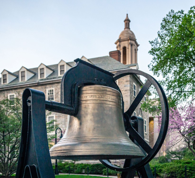closeup of the Willard Bell outside Old Main with flowering trees in the background by Nick Sloff '92 A&A