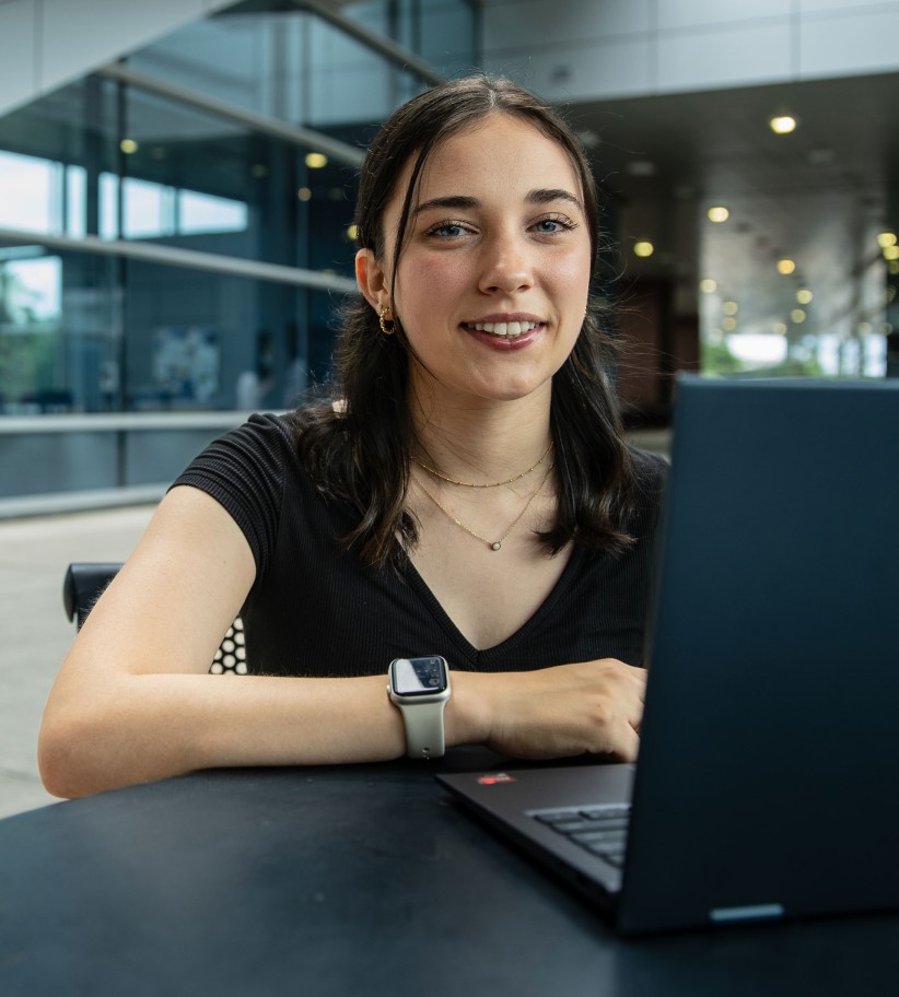 Hailey Onweller sitting at a table with her laptop, photo by Cardoni