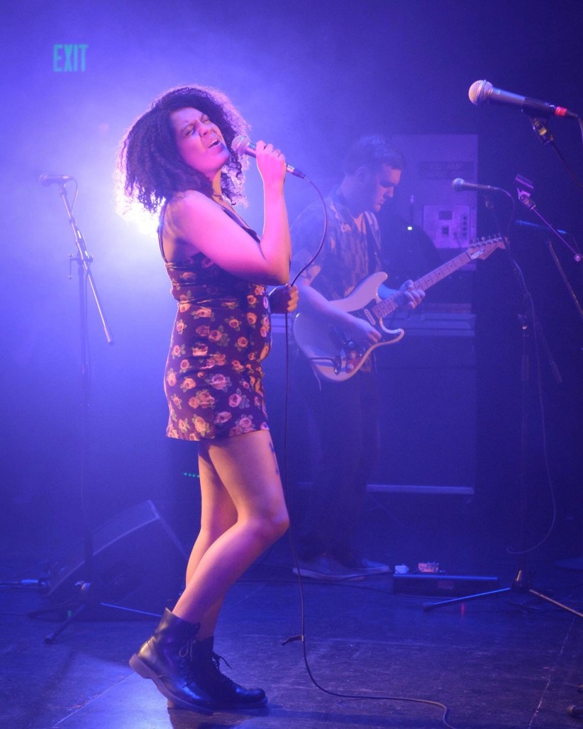Kat Leverenz singing on a purple-lit stage, courtesy