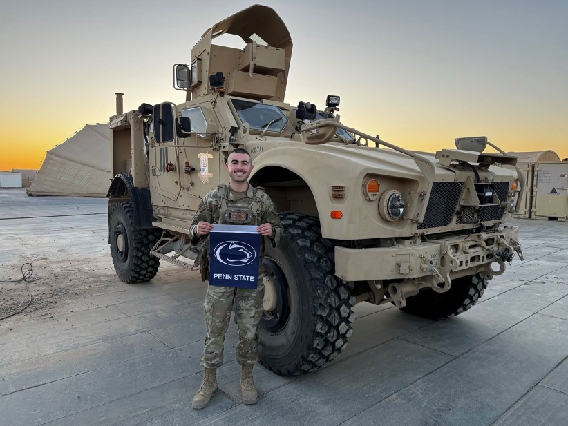 photo of Senior airman Alexander Dugan holding a Penn State flag in front of an army vehicle, courtesy
