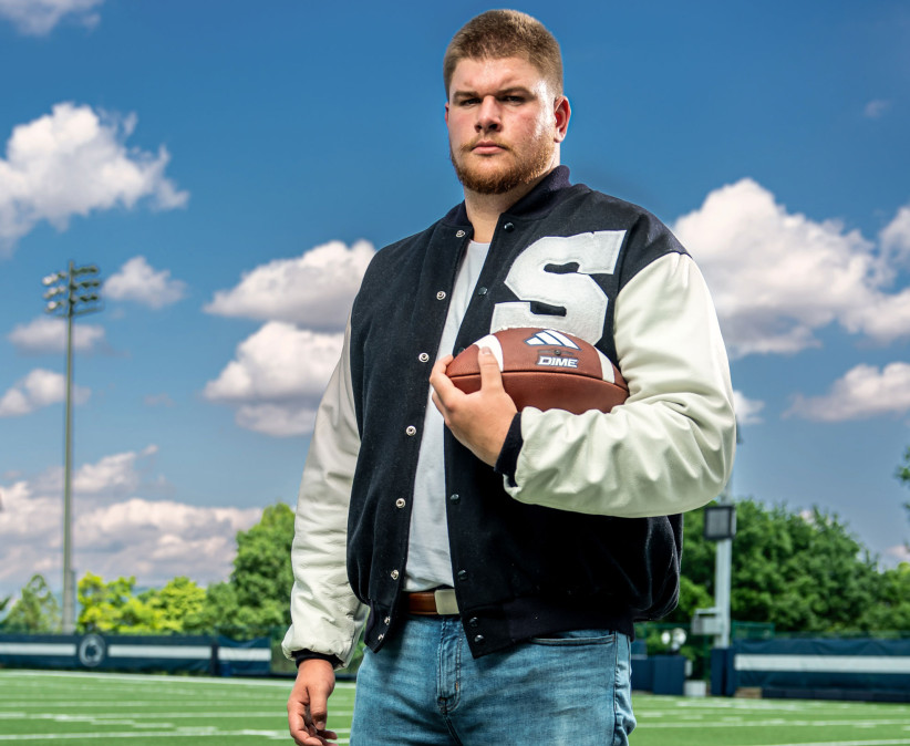 Cousins in letterman jacket holding football on the field, photo by Cardoni