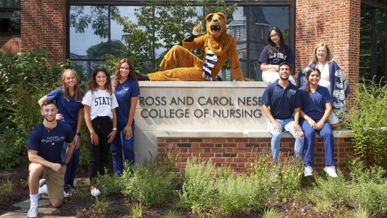 photo of students and Nittany Lion posing in front of the Ross and Carol Nese College of Nursing sign