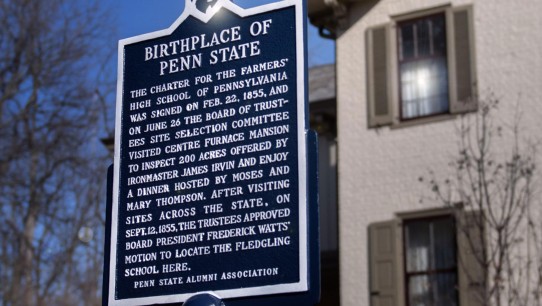 Penn State historical marker sign reading "Birthplace of Penn State" with building and blue sky in background, by Patrick Mansell