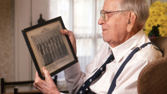 photo of White looking at a framed photo of former Penn State colleagues by Steve Tressler