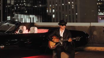 Gene Woods playing guitar in front of sportscar