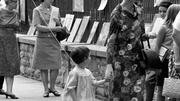 Black and white photo of a woman and child holding hands walking down a street during Arts Fest, by Penn State Archives