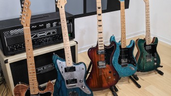 five colorful electric guitars on stands in front of an amp with a color block wall behind them, courtesy Anthony Robinson