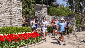 photo of Paul Johnson running through the gates below Old Main onto College Ave with other runners behind him by Nick Sloff '92 A&A