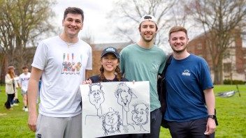 four students hold up a caricaturist's rendering of them during PS "I Heart U" Week's Old Main open house, by Penn State Alumni Association