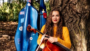 Ruth Stokes sitting outside against a tree with her cello, photo by Cardoni