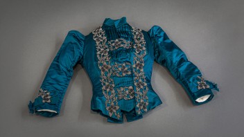 photo of a peacock blue silk-satin dinner jacket with intricate beadwork and a banded collar with pleating on the bust, garment from the Penn State Fashion Archive photographed by Nick Sloff '92 A&A