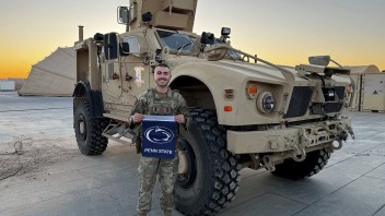 photo of Senior airman Alexander Dugan holding a Penn State flag in front of an army vehicle, courtesy