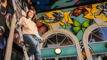 photo of Guo standing on a ladder in a room painted with her murals, by Cardoni