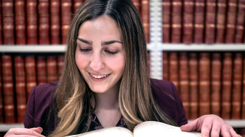 photo of Miller looking at a thick book in front of bookshelves, courtesy